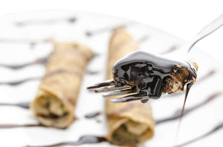 Piece of  pancake on a fork with liquid chocolate dropping down of  it  Blurred plate of pancakes in background の写真素材
