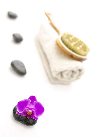 Spa setting with pink orchid and defocused massage stones, brush and a towel 