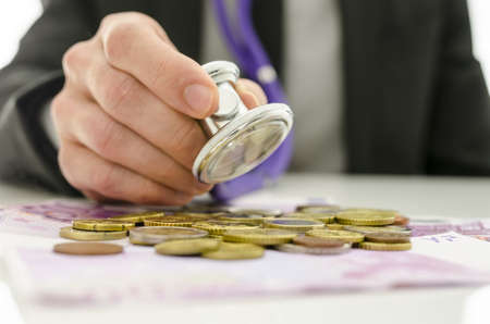 Closeup of businessman checking Euro coins and banknotes with stethoscope. Concept of financial...