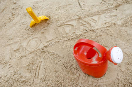 Word holidays written in sand with beach toys next to it.の写真素材