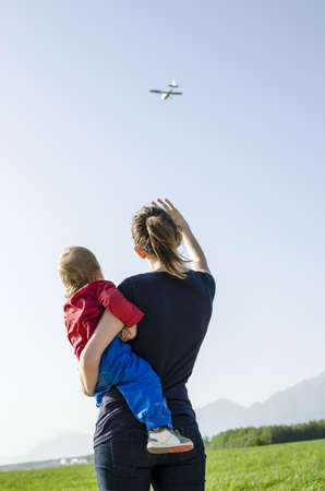 Back view of mum holding her son waving at airplane の写真素材