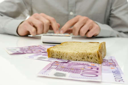 Slice of bread on Euro banknotes with male hand calculating food expenses in background. の写真素材