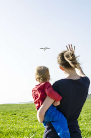 Mum carrying her son and waving at airplane.の写真素材