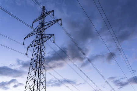 Electric tower and wires against cloudy sky at dusk.