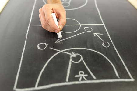 Closeup of basketball coach drawing game strategy on black board.