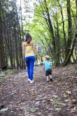 Rear view of young mother and her toddler son spending quality time together walking in the woods.