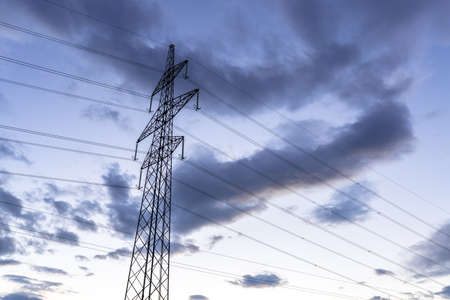 High voltage electric tower over cloudy sky at dusk.