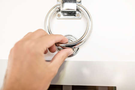 Closeup of male hand knocking on modern white front door with door knocker.
