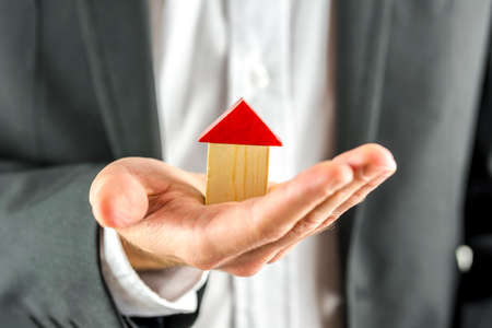 Closeup of real estate agent holding a wooden  house in his hand. Real estate business. の写真素材