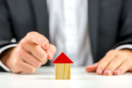 Closeup of real estate agent pointing to a wooden house.