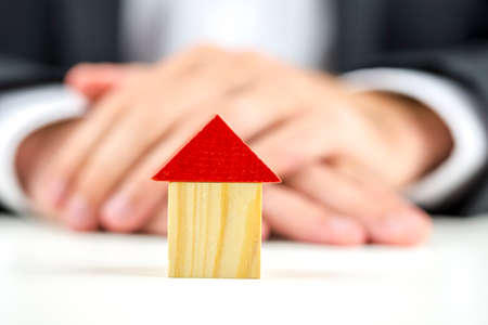 Closeup of real estate agent sitting at his desk with wooden toy house in front of him.の写真素材