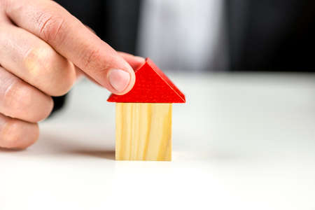 Businessman putting a roof on a wooden toy house.の写真素材