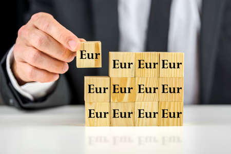 Closeup of businessman putting together many wooden cubes with Eur written on them. の写真素材