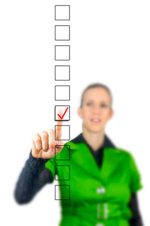 Woman ticking a check box in a vertical line of empty boxes in a survey or questionnaire on a virtual screen or interface with her fingerの写真素材