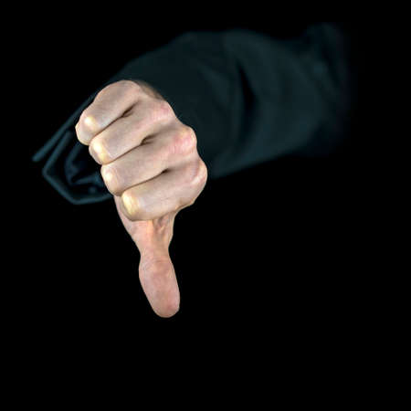 Close-up of a hand with black sleeve showing the thumb down, gesture of disapproval, isolated on black backgroundの写真素材