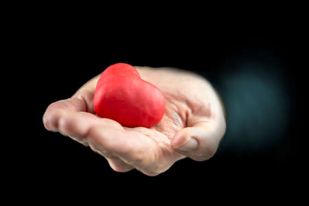 Man cupping a red heart in his hand as he offers it as a gift to a sweetheart symbolic of love and romance and a Valentines Day wishの写真素材