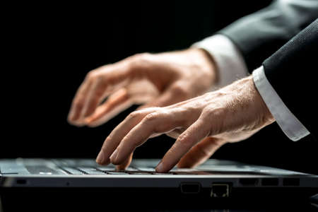 Close up view over a dark background of the hands of a businessman typing on his laptop computer entering data or surfing the internet onlineの写真素材