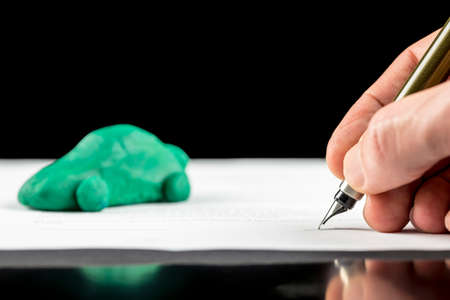 Conceptual image of the hand of a man signing a contract for the lease or purchase a green eco-friendly fuel efficient, electric or hybrid car with reduced carbon emissionsの写真素材