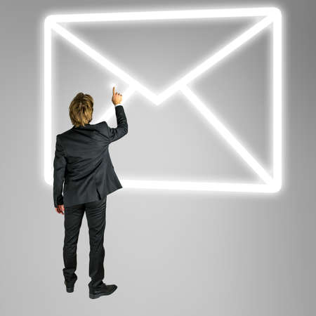 Businessman standing in front of an envelope mail icon on a virtual screen or interface conceptual of online contact and communicationの写真素材