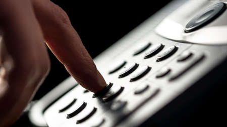 Closeup of the finger of a businessman making a call on a landline telephone pressing the buttons on...