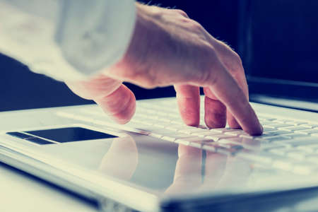 Closeup of the hands of a man typing on a laptop keyboard as he enters information or surfs the internet in an online communication and contact concept. With retro filter effect.の写真素材