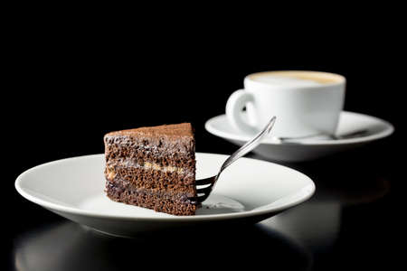 Slice of delicious fresh chocolate cake served with a cup of aromatic cappuccino coffee on a dark with copyspace.の写真素材