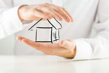 Man protecting a hand sketched outline of a house with his hands conceptual of ownership, insurance, security and risk, closeup of his hands against his white shirt.の写真素材