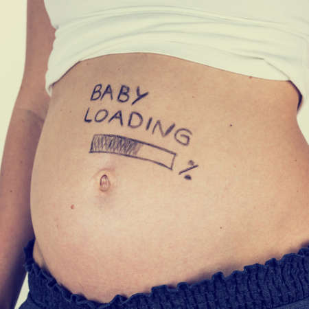 Bare swollen belly of a pregnant young woman with the handwritten words - Baby Loading - and a bar below showing the percentage marking the advancing stages of her pregnancy, toned retro effect.の写真素材