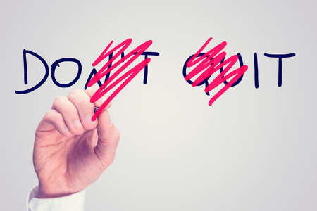 Dont Quit - Do It, conceptual image with a man scrubbing through letters in the words Dont Quit converting them to Do It with a red pen in a motivational message of hope and perseverance.