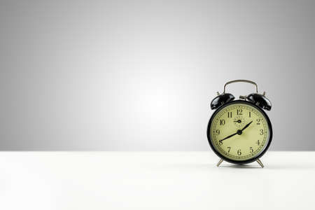Vintage style metal alarm clock with bells standing on a white counter against a graduated grey...