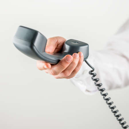 Closeup of male hand holding telephone handset towards you.の写真素材