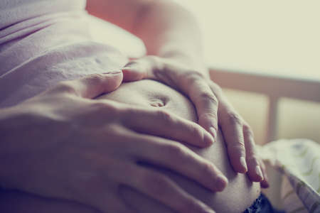 Closeup of pregnant woman holding her hands on her swollen belly shaping a heart, toned retro 