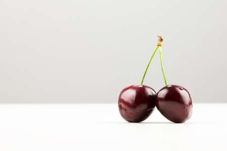 Two ripe red juicy cherries on a joined stalk on bright background.の写真素材