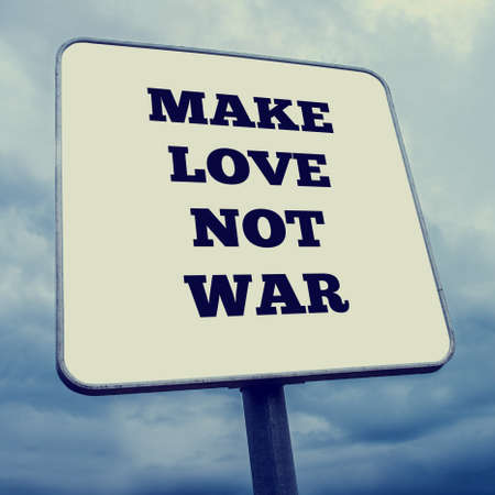 White rectangular signpost with the words - Make Love Not War - against a cloudy blue sky viewed at an oblique angle.の写真素材