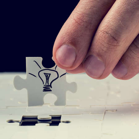 Male hand inserting the final missing puzzle piece with light bulb drawn on it. Concept of innovation or getting a business idea.の写真素材