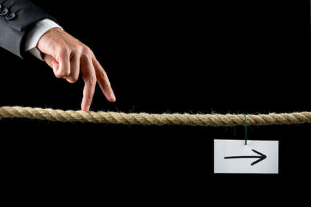 Conceptual image of business determination with a businessman walking his fingers along a length of rope towards a white card with right pointing arrow.の写真素材
