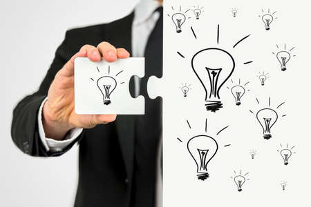 Businessman with the idea for business development holding a puzzle piece with lightbulb on it to...