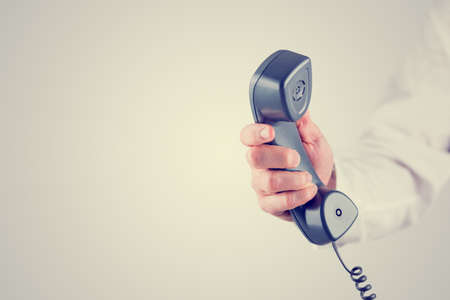 Retro effect faded and toned image of a male hand holding landline telephone receiver with empty space ready for your text.の写真素材