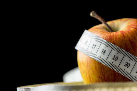 Close-up of a fresh tasty apple, natural source of vitamins and minerals, wrapped with a white measuring tape, with copy space on black, concept of dieting and healthy nutritious food の写真素材