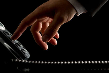 Close-up of the hand of a businessman dialing or initiating a phone call by operating the keypad of a desk corded land line telephone, on black の写真素材