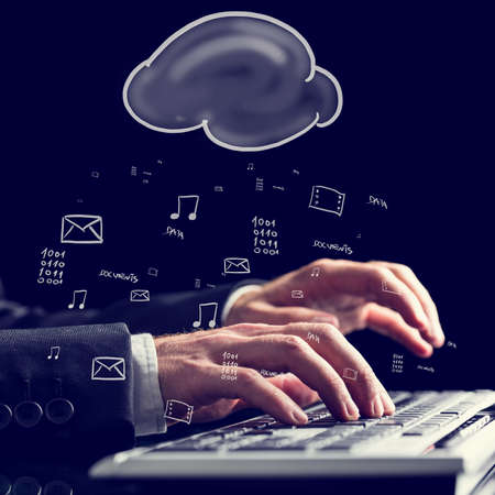 Businessman typing on a computer keyboard against a background of a blackboard with hand-drawn application icons and a cloud conception of cloud storage and computing.の写真素材