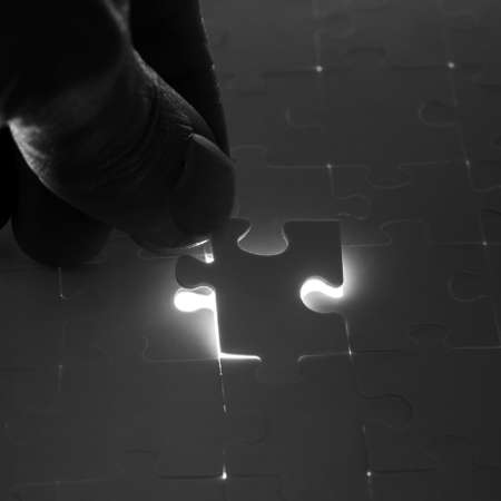 Man completing a jigsaw puzzle placing the last piece in position over the remaining gap with light...