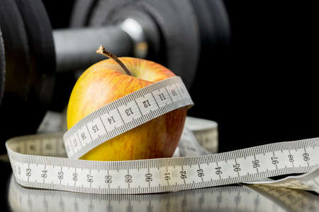 Fresh juicy apple wrapped in a tape measure with a gym weight visible behind conceptual of a healthy diet and nutrition , exercise , fitness and weight loss.の写真素材