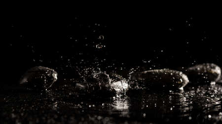 Dark atmospheric image of pure fresh water splashing on smooth black basalt spa stones conceptual of...