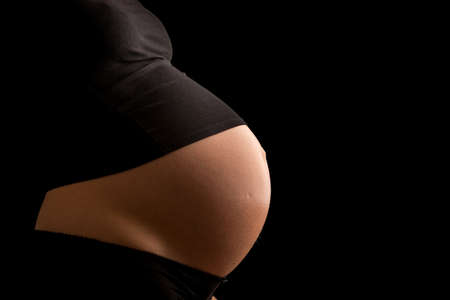 Exposed pregnant stomach of an expectant mother on black background.の写真素材