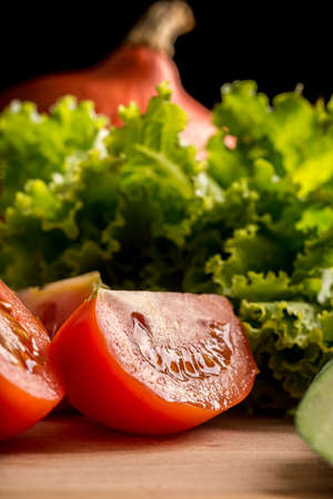 Low angle view with texture of a fresh juicy ripe red sliced tomato on a wooden chopping board with fresh leafy green lettuce for making a healthy saladの写真素材