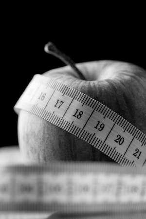 Tape measure wound around an apple in a black and white diet, health, weight loss and fitness...