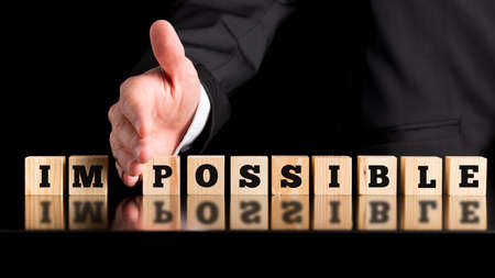 The word Im - Possible on a line wooden blocks separated by the hand of a businessman conceptual of all things being possible given enough input and effort, on a dark background with copyspace.の写真素材