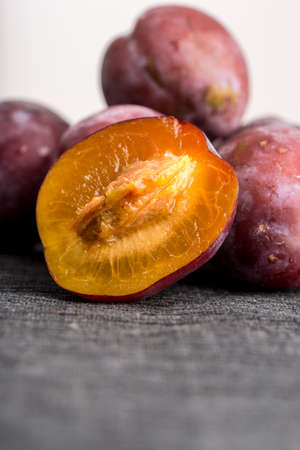 Fresh ripe halved plum showing the golden flesh and stone or pip with a pile of purple plums behind and foreground copyspace.の写真素材