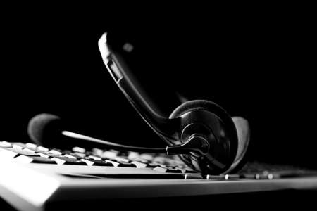 Low angle conceptual black and white image of a headset lying on a computer keyboard against a dark...
